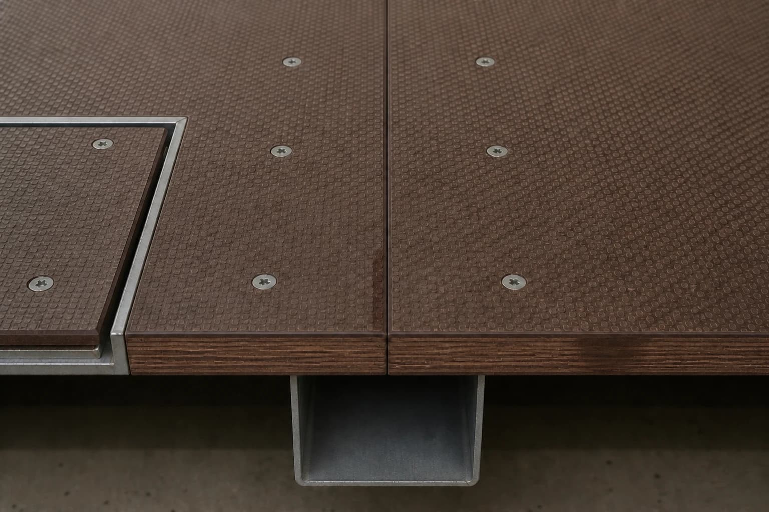 Close-up of two level anti-slip plywood panels supported at a uniform joint, with flush fasteners, thin patterned film and dark resin-sealed cut edges