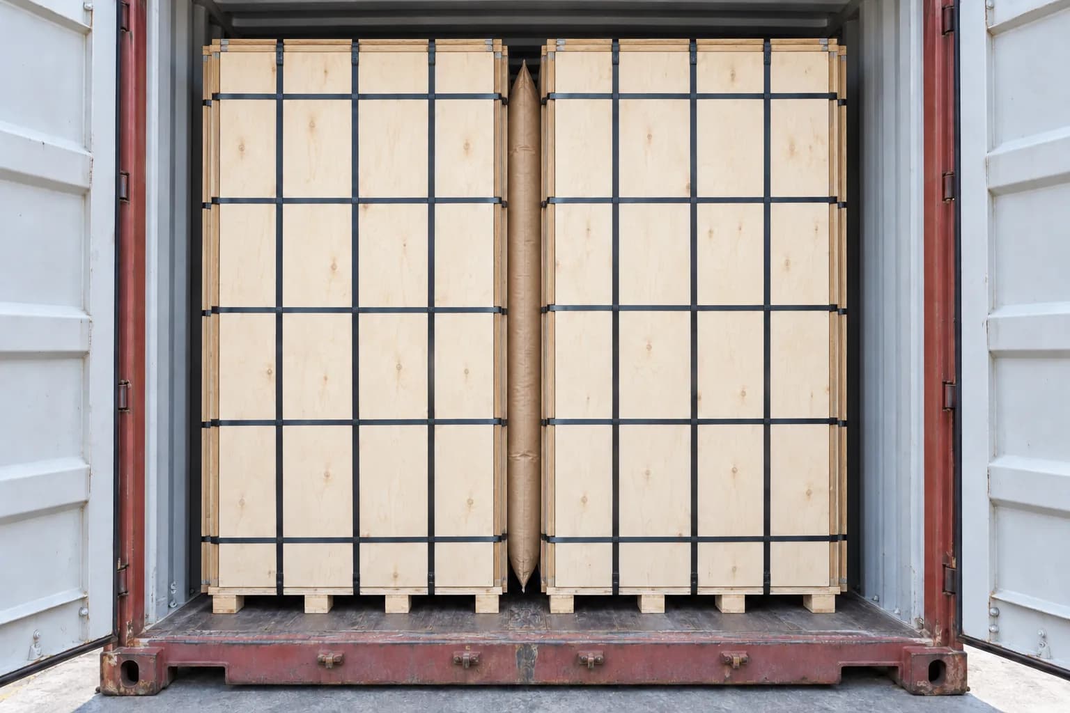 Two large vertical plywood pallet packs nearly filling a tall freight container with a slim central dunnage airbag