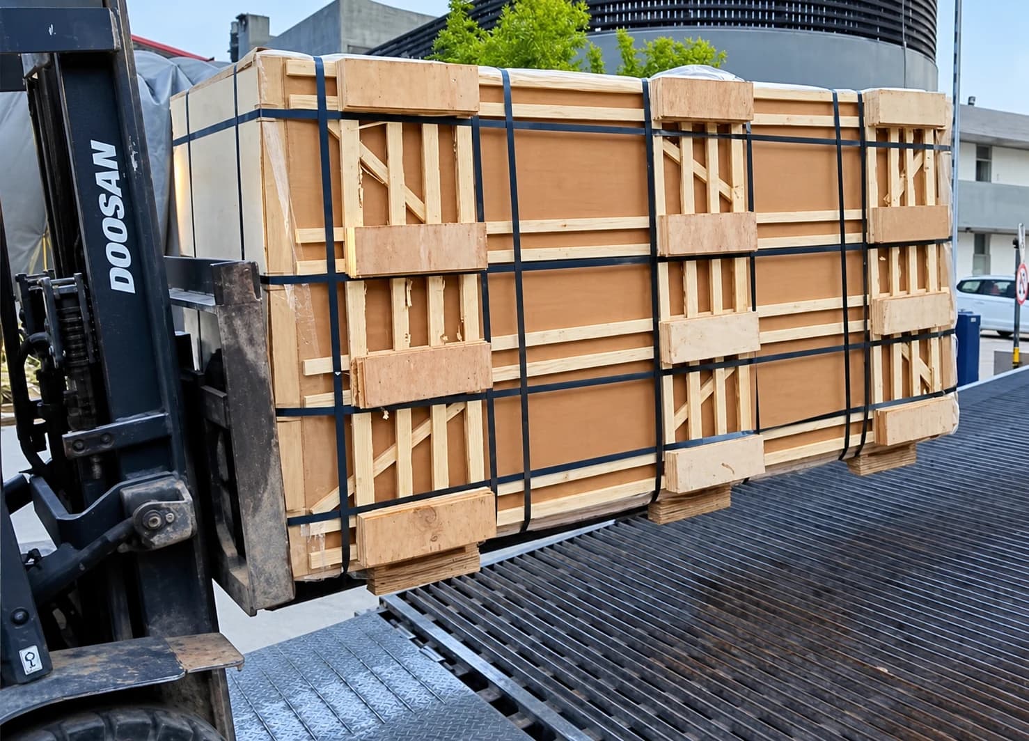 Crated plywood bundle carried by a forklift at a loading platform.
